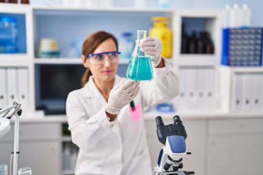 Middle age woman wearing scientist uniform measuring liquid at laboratory