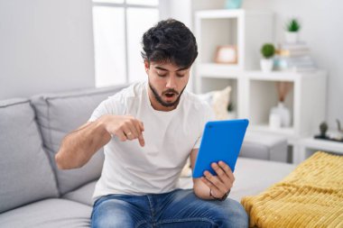 Sakallı İspanyol bir adam kanepeye oturmuş parmaklarını göstererek reklamını yapıyor, şaşırmış yüzünü ve ağzını açıyor. 