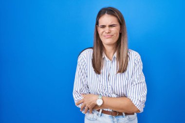 Hispanic young woman standing over blue background with hand on stomach because nausea, painful disease feeling unwell. ache concept. 