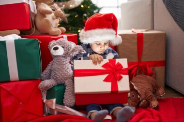 Adorable toddler unpacking christmas gift sitting on floor at home