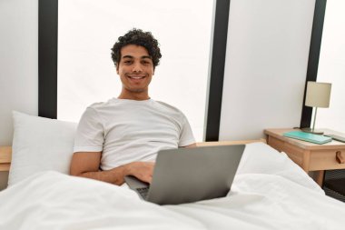 Genç İspanyol adam yatak odasında dizüstü bilgisayar kullanıyor..