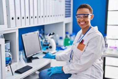 Afrikalı Amerikalı bilim kadını laboratuvarda bilgisayar kullanarak gülümsüyor.