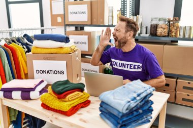 Middle age man wearing volunteer t shirt working with laptop shouting and screaming loud to side with hand on mouth. communication concept. 