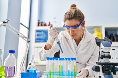 Laboratuvarda pipet kullanan bilim adamı üniforması giyen genç sarışın kadın.