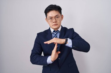 Young asian man wearing business suit and tie doing time out gesture with hands, frustrated and serious face 