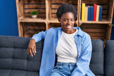 Afro-amerikalı bir kadın evdeki koltukta kendinden emin bir şekilde oturuyor.