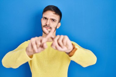 Latin kökenli bir adam mavi arka planda duruyor. Reddedilme ifadesi negatif işaret veriyor. 