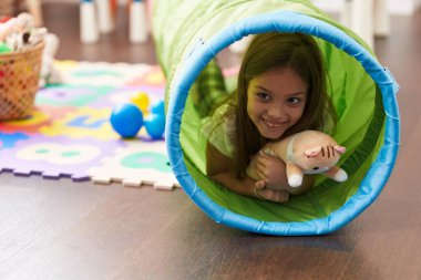 Adorable hispanic girl crawling inside tunnel toy at kindergarten
