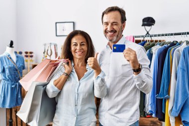 Alışveriş torbaları ve kredi kartı tutan İspanyol orta yaşlı çift elleriyle mutlu bir jest yapıyor. Kameraya bakıp başarıyı gösteren ifade. 