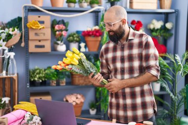Young bald man florist holding bouquet of flowers at flower shop