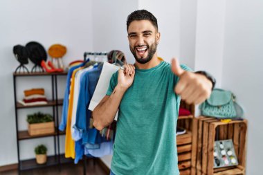 Satış mağazasında sakallı, alışveriş torbası tutan, elinde olumlu bir jest yapan, gülümseyen ve başarı için sevinen genç yakışıklı bir adam. kazanan jest. 