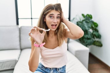 Genç sarışın kadın, görünmez hizayı tutuyor, ortodontik deli ve elleri başının üstünde korkmuş, korkmuş ve ağzı açık şoktan şaşırmış. 