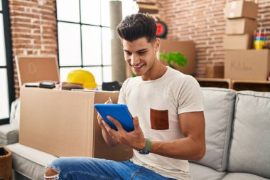 Yeni evindeki koltukta oturan dokunmatik ped kullanan İspanyol genç adam.