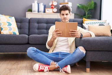 Genç İspanyol adam evde oturmuş kitap okuyor.