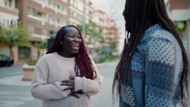İki Afro-Amerikalı arkadaş gülerek sokakta bir arada duruyorlar.