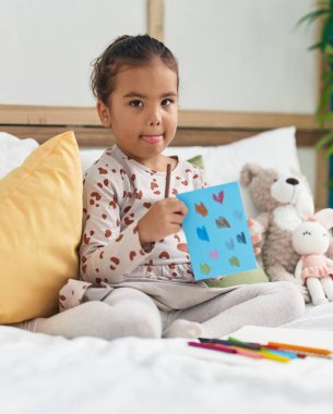 Yatak odasına oturmuş defterine resim çizen sevimli İspanyol kız.