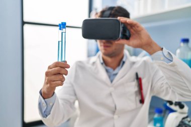Genç İspanyol bilim adamı laboratuvarda test tüpleri tutarken sanal gerçeklik gözlüğü kullanıyor.