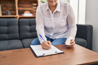 Orta yaşlı kadın psikolog, psikoloji merkezinde reçete yazıyor.