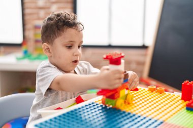 Adorable hispanic toddler playing with construction blocks sitting on table at kindergarten