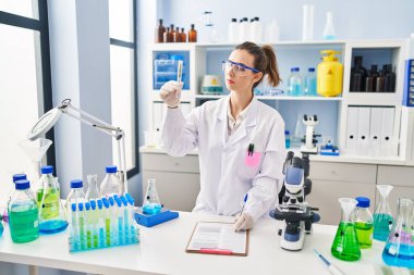 Young woman wearing scientist uniform analysing herb at laboratory