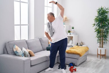 Orta yaşlı, kır saçlı, evinde gerinen bir adam.