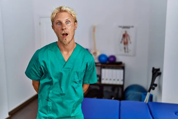 Young Blond Man Wearing Physiotherapist Uniform Standing Clinic Afraid Shocked — Stockfoto