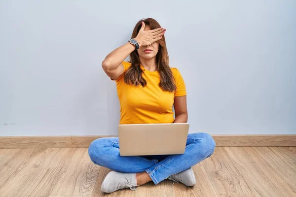 Hispanic Woman Using Laptop Sitting Floor Home Covering Eyes Hand —  Fotos de Stock