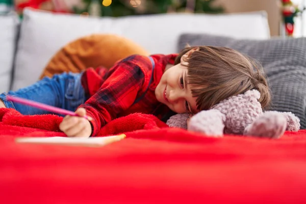 可爱的幼儿在笔记本上写字 躺在家里的圣诞树旁的沙发上 — 图库照片