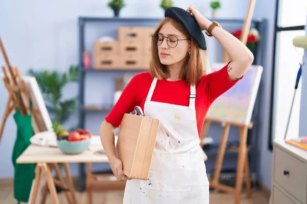 Young Redhead Woman Art Studio Holding Art Case Confuse Wondering — Foto Stock