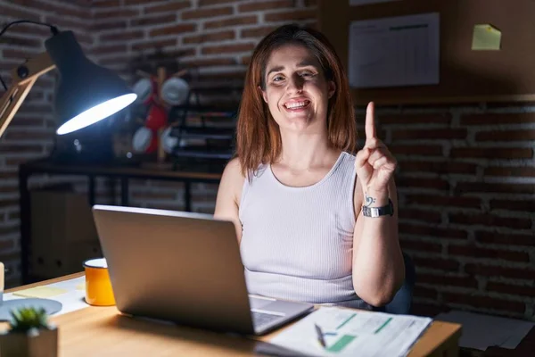 自信と幸せ笑顔ながら夜のオフィスで働くブルネットの女性は指の第1位を示し 指摘します — ストック写真