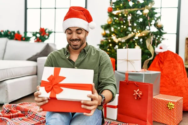 Young Hispanic Man Unboxing Gift Sitting Floor Christmas Tree Home — Stock Photo, Image