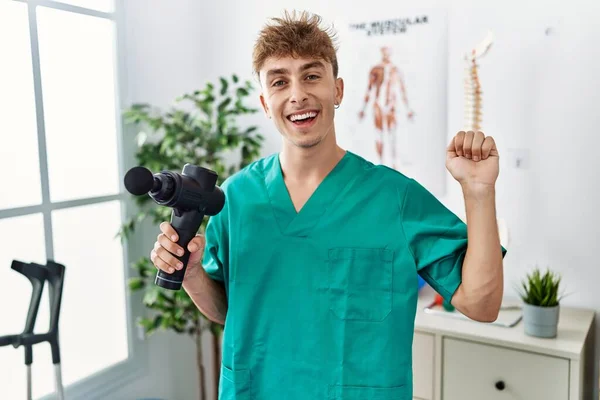 Young Caucasian Physio Man Holding Muscle Percusion Gun Clinic Celebrating — Stok fotoğraf