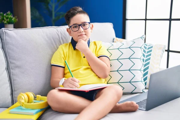 Young Hispanic Kid Doing Homework Sitting Sofa Hand Chin Thinking — Stok fotoğraf