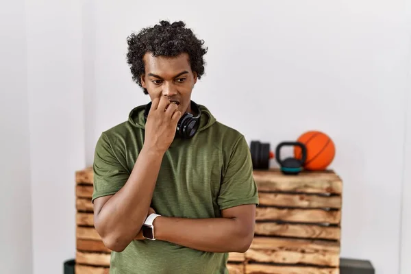 ジムでスポーツウェアを身に着けている巻き毛を持つアフリカ人男性は 口の爪をかむ上で手で強調し 緊張している 不安の問題 — ストック写真