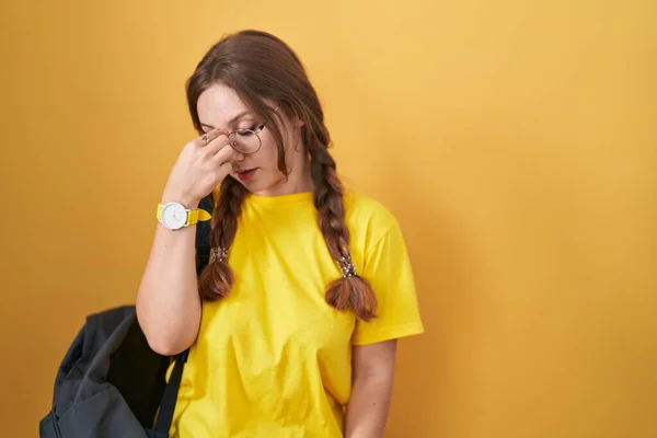 年轻的高加索女人背着学生背包 背着黄色的背景 疲惫地揉揉鼻子和眼睛 感觉疲劳和头痛 压力和挫败感概念 — 图库照片