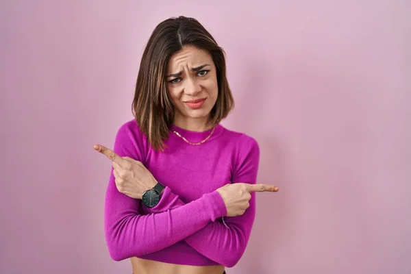 西班牙女人站在粉红的背景上 手指指向两边 方向不同 — 图库照片