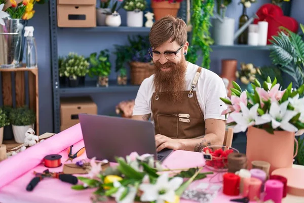 Young redhead man florist smiling confident using laptop at flower shop