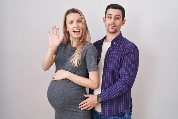 Young Couple Expecting Baby Standing White Background Waiving Saying Hello — Stock Photo, Image