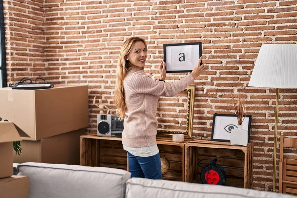 Young Woman Smiling Confident Hanging Picture Wall New Home — Stockfoto