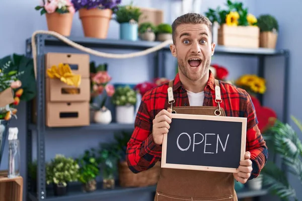 Young caucasian man working at florist holding open sign celebrating crazy and amazed for success with open eyes screaming excited.