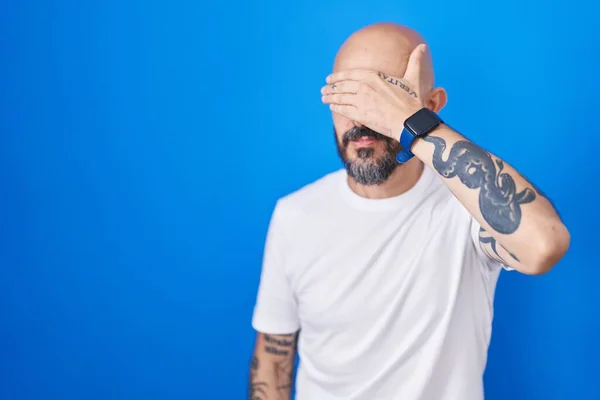 有纹身的西班牙男人站在蓝色的背景上 用手捂住眼睛 看起来严肃而忧郁 躲藏和拒绝的概念 — 图库照片