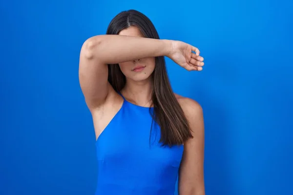 Mulher Hispânica Sobre Fundo Azul Cobrindo Olhos Com Braço Olhando — Fotografia de Stock