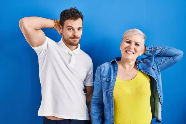 若いブラジル人の母親と息子が青い背景の上に立ってリラックスしてストレッチ 腕と手頭と首の後ろに笑顔幸せ — ストック写真