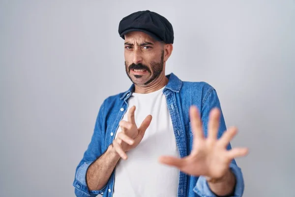 Hispanic man with beard standing over isolated background disgusted expression, displeased and fearful doing disgust face because aversion reaction.