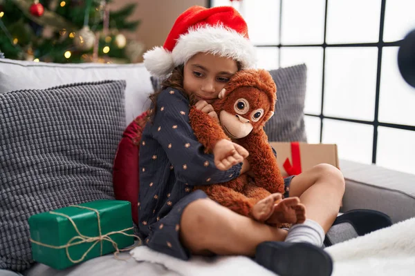 Adorable Hispanic Girl Hugging Monkey Doll Sitting Sofa Christmas Tree — 스톡 사진