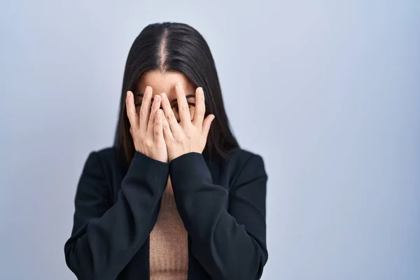 stock image Young brunette woman standing over blue background with sad expression covering face with hands while crying. depression concept. 