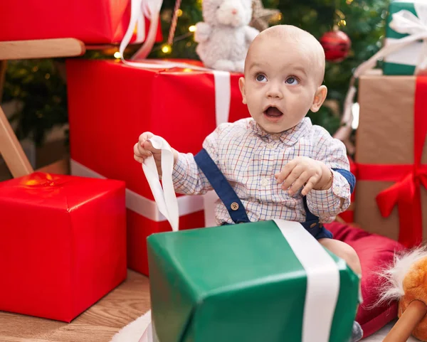 可爱的高加索婴儿打开包装礼物坐在地板上的圣诞树旁 — 图库照片