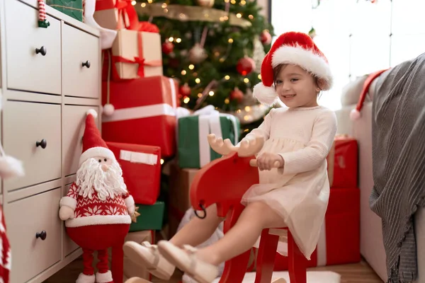 可爱的女孩坐在家里的圣诞树旁摇动驯鹿 — 图库照片