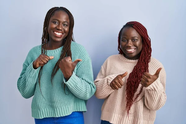手と親指を上げて後ろを指差す青い背景のアフリカ人女性二人が自信を持って微笑んだ — ストック写真