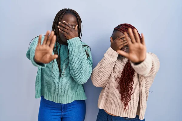 両手で目を覆い 悲しみと恐怖の表情でストップジェスチャーを行う青い背景の上に立つ2人のアフリカ人女性 恥をかかせ否定的な概念 — ストック写真